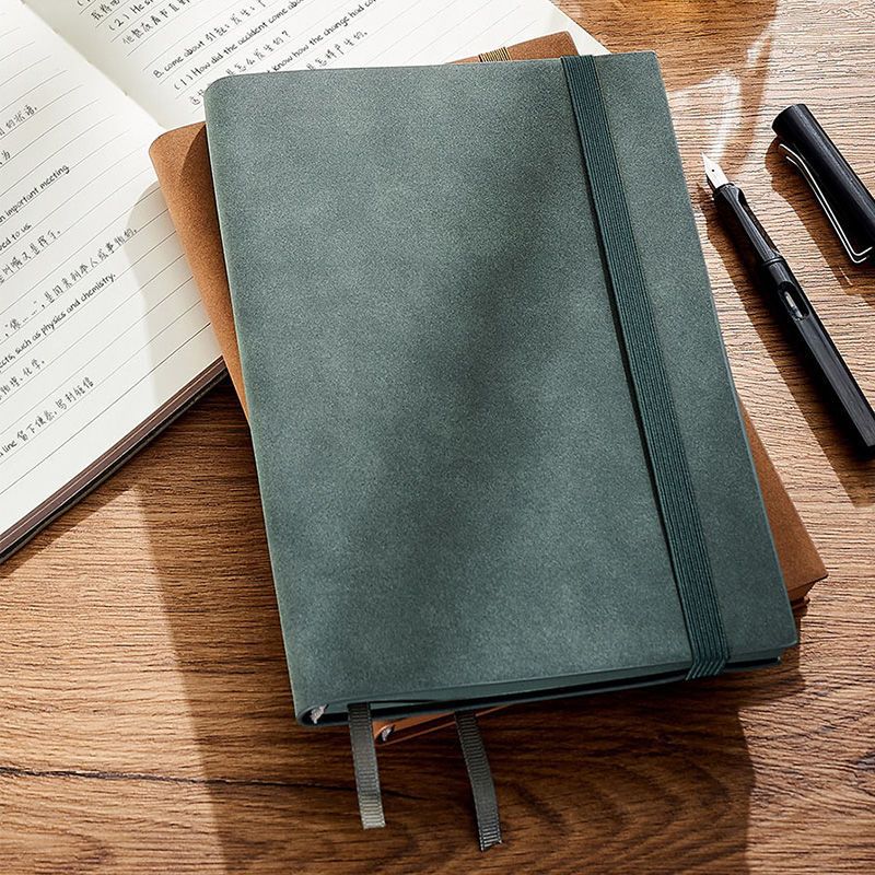 Green notebook with an elastic closure on a wooden desk